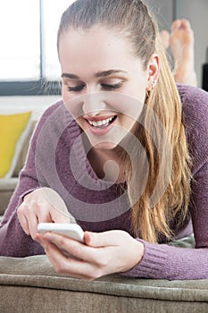 Laughing gorgeous teenage girl connected to her smartphone text messaging