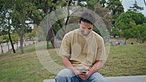 Laughing guy reading cellphone message on park bench closeup. Happy hispanic man