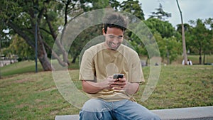 Laughing guy reading cellphone message on park bench closeup. Happy hispanic man