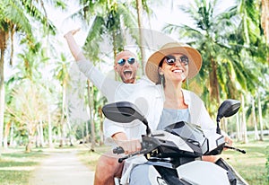 Laughing happy couple travelers riding motorbike during their tropical vacation under palm trees. Man emotionally raised hand up photo
