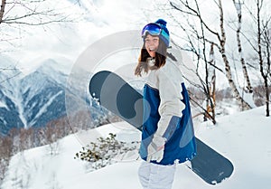 Laughing happy girl with a snowboard and background of mountains and snowy trees