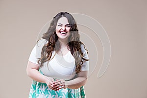 Laughing happy plus size model in casual clothes, fat woman on beige background