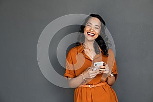 Laughing happy smiling woman messaging on mobile phone on gray wall