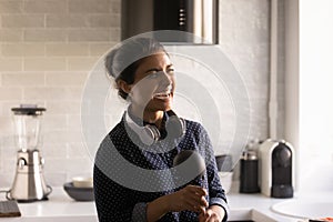 Laughing hindu woman in wireless headphones singing karaoke at kitchen