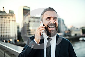 Laughing hipster businessman with smartphone in the city, making a phone call.