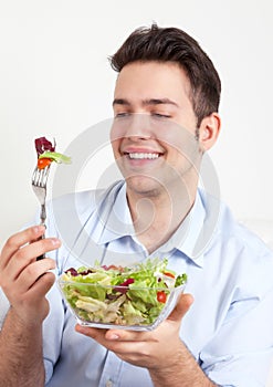 Laughing hispanic guy on a sofa loves green salad