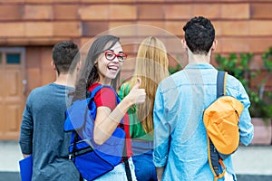 Laughing italian female student showing thumb up with group of other students