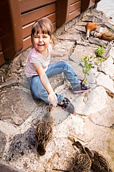 Laughing kid girl feeding ducks with hands