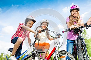 Laughing kids in helmets hold bike handle-bars