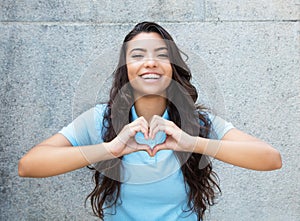Laughing latin american woman in love showing heart with hands