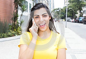 Laughing latin woman with yellow shirt at phone in city
