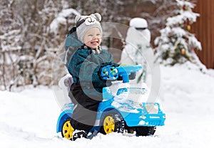 Laughing little boy drives toy car on snow