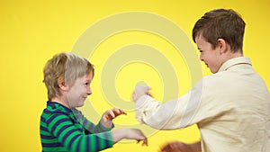 Laughing little brothers having fun fighting at yellow background. Positive Caucasian boys imitating fight. Relaxation