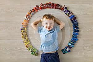 Laughing little cute baby boy lying in circle of car model toys hot wheels collection top view