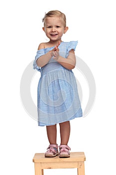 Laughing little girl in blue dress is clapping her hands