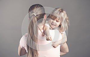 Laughing little girl looks happy in mother`s arms Beautiful baby girl pulls mom`s hair and smiling. Woman holding her
