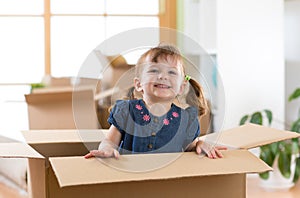 Laughing little girl sitting inside cardboard boxe in her new home
