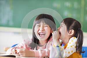 Laughing little girls sharing secrets in class