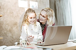Laughing long-haired little girl being interested in work of her mother