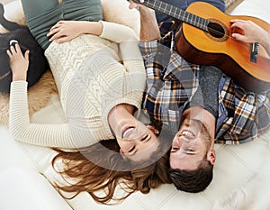 Laughing and loving the music. a young man playing guitar while lying on the floor with his girlfriend. photo