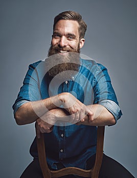 Laughing man with arms on back of chair over gray