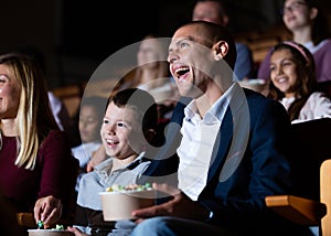 Laughing man with preteen son watching comedy movie in cinema