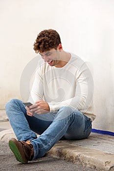 Laughing man sitting on ground with mobile phone