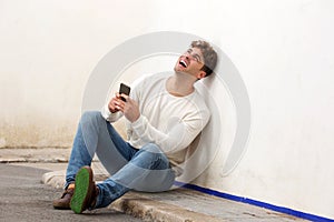 Laughing man sitting on sidewalk with mobile phone