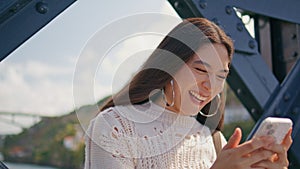 Laughing model reading sms on bridge closeup. Funny girl typing mobile phone