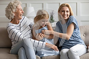 Laughing mommy and granny tickling with little girl on couch