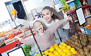 Laughing mother and daughter buying fruits