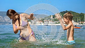 Laughing mother and her son, enjoying playful splashes by the sea. Family togetherness, vacation delights, and the