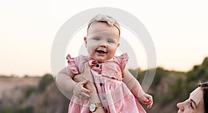 Laughing mother lifting her adorable baby daughter in air. Baby is looking at the camera and smiling. Happy family