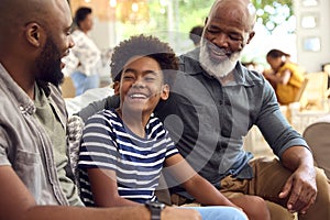 Laughing Multi-Generation Male Family Hanging Out On Sofa At Home Talking Together