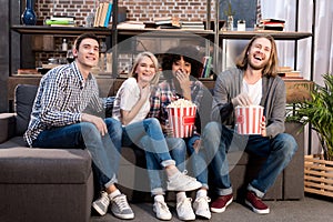 Laughing multicultural friends watching movie on sofa