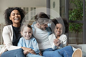 Laughing multiracial couple enjoying watching television funny films with kids.