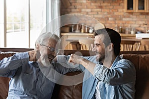 Laughing old father bumping fists with adult son
