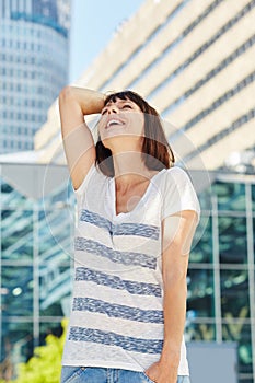 Laughing older woman with hand in hair standing in city