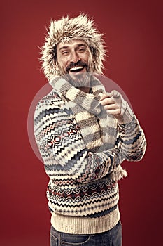 Laughing out loud. Bearded man accessorizing sweater with hat and scarf. A winter ensemble protects him from cold