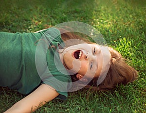 Laughing playful crazy crying kid girl lying on the grass on nature summer background. Closeup