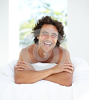 Laughing, portrait and a handsome man in bed for sleep, relaxing and rested in the morning. Wake up, resting and a guy