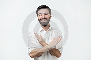 Laughing positive spanish guy dressed in white shirt showing stop gesture, asking to stop joking.