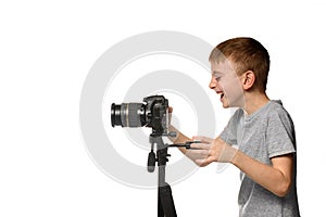 Laughing schoolboy shoots video on DSLR camera. Side view. White background, isolate