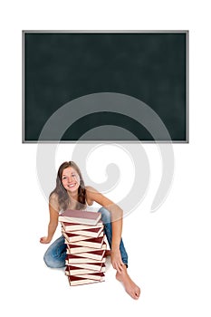Laughing schoolgirl with a huge pile of books in front of an emtpy blackboard
