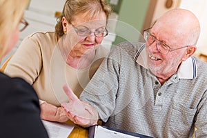Laughing Senior Adult Couple Going Over Documents in Their Home with Agent At Signing
