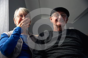 Laughing Senior Couple Sitting On Sofa At Home Watching Television Together