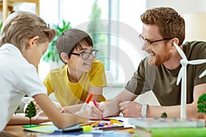 Laughing short-haired man in clear glasses helping little boys