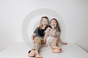 Laughing siblings sitting together on table. Boy hugs girl, she leans away a bit