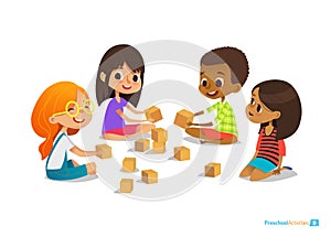 Laughing and smiling kids sit on floor in circle, play with toy cubes talk.