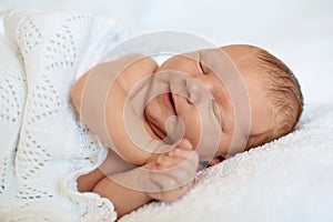 Laughing, smiling little newborn baby boy sleeping in white bla